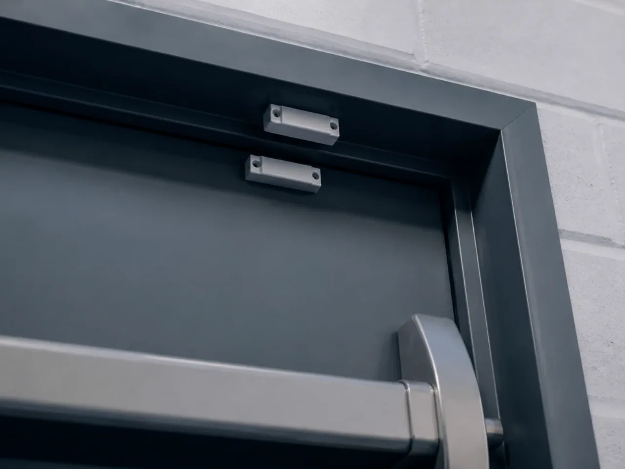 Porte métallique d'issue de secours avec un contact d'ouverture blanc sur le dormant et une barre antipanique