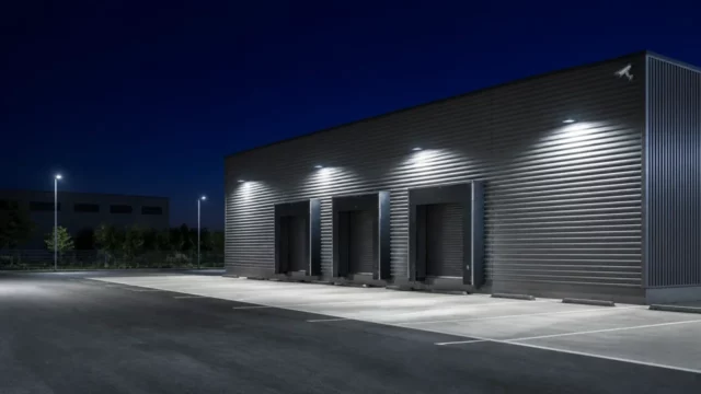 Entrepôt logistique de nuit éclairé par des projecteurs, quais fermés et caméra fixée en haut de la façade