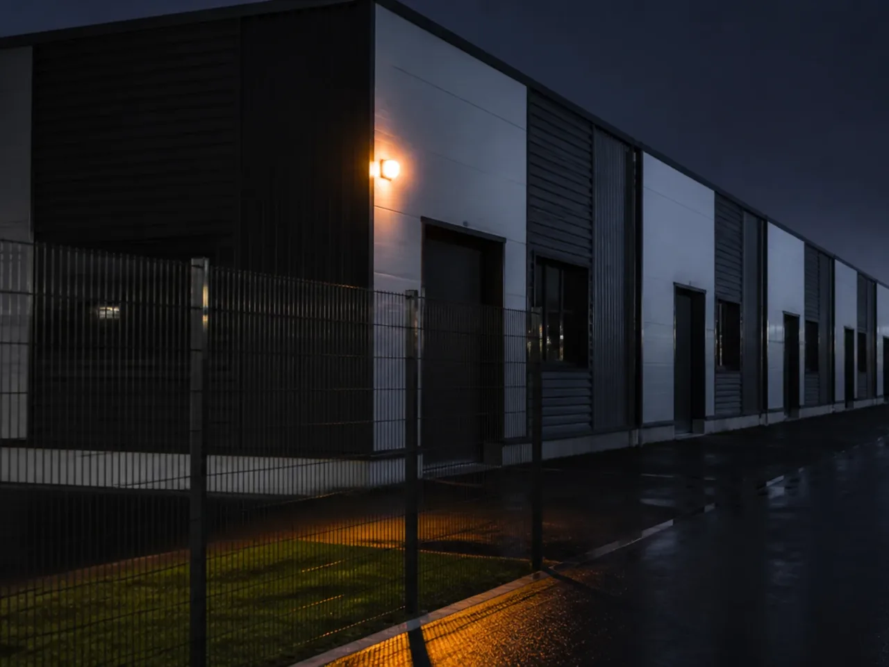 Rangée de cellules d'activité identiques derrière une clôture, un seul flash orange allumé sur une façade la nuit